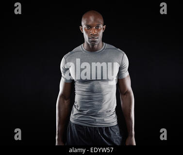 Portrait of fit young man with muscular build standing against black background. Afro American fitness model. Stock Photo