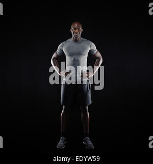 Full length image of happy young man standing on black background. Muscular African athlete in sportswear. Stock Photo