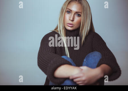 Portrait of pretty young woman sitting on floor staring at camera. Caucasian female model wearing sweater looking at camera. Stock Photo