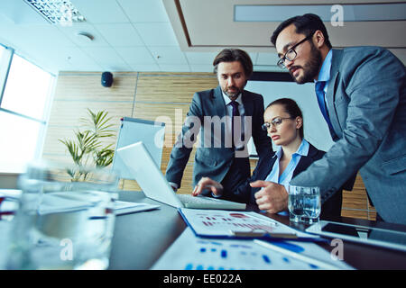 Team of three workers looking at laptop screen Stock Photo
