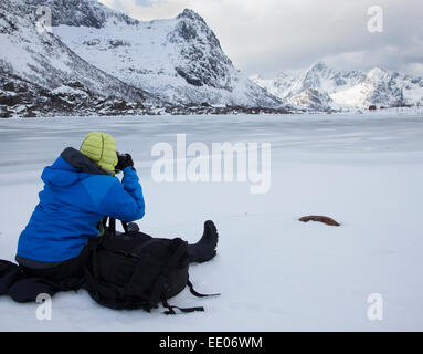 Photographer beside frozen lake in Lofoten Islands, Norway with snowy mountains in distance. Stock Photo