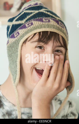 Attractive Teenage Boy with Autism and Downs Syndrome is Laughing as he puts on his winter wool hat Stock Photo