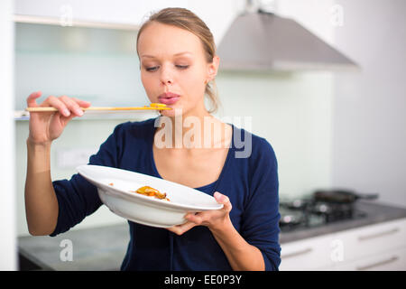 Pretty, young woman cooking a diner in a modern kitchen, tasting the food she made Stock Photo