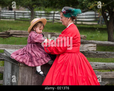 A helping hand from Grandmother. A young child in a straw hat is helped by her grandmother as she sits near a split-rail fence Stock Photo