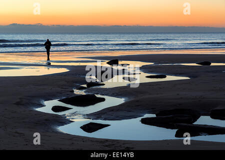 Man walking on beach at low tide at sunset, Southerndown, Wales, UK Stock Photo