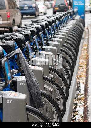 Unused citi rental bikes in the rain. A row of citibikes locked into their racks  along a NYC street.  A grey scarf hangs. Stock Photo