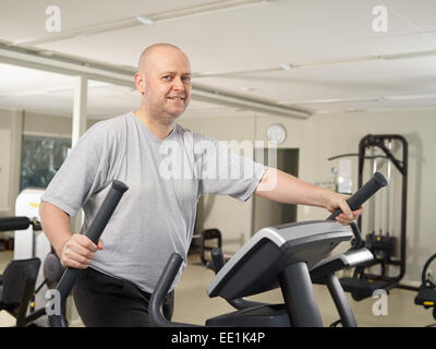 Mature man takes care of his health and he use elliptical trainer in the gym Stock Photo