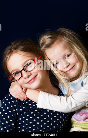 Portrait of two cute girlfriends or sisters, vertical studio shot with blue background Stock Photo