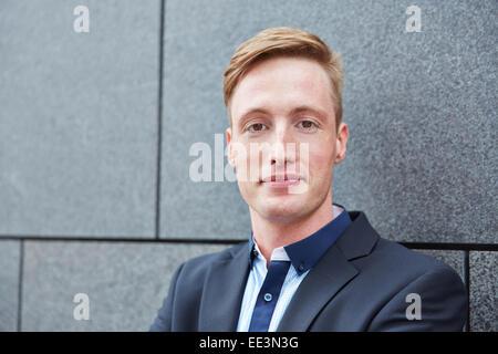 Young smiling business man standing outdoors next to a wall Stock Photo