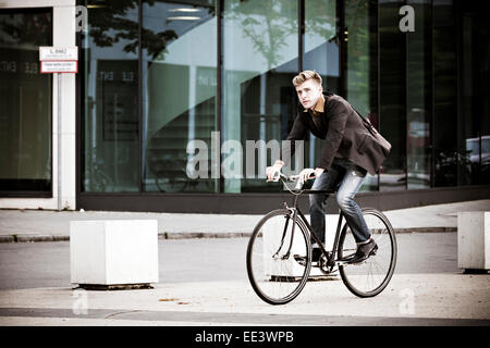 Young businessman riding bicycle on city street Stock Photo
