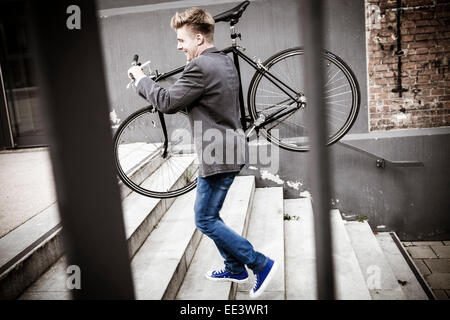 Young businessman carrying bicycle across steps, Munich, Bavaria, Germany Stock Photo