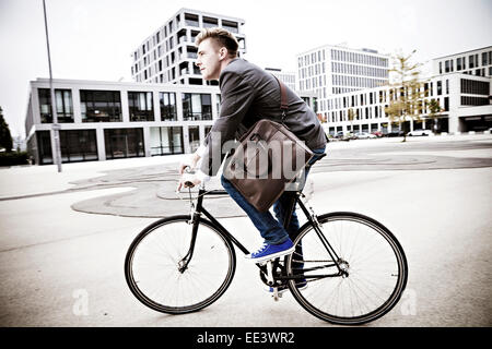Young businessman riding bicycle, Munich, Bavaria, Germany Stock Photo