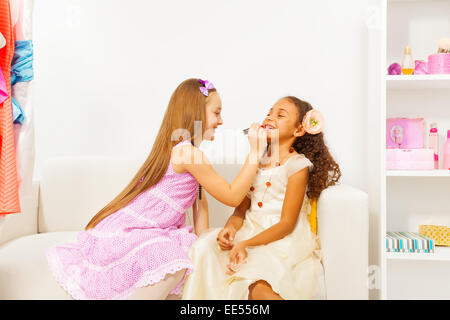 Girl with long hair applies lipstick on her friend Stock Photo