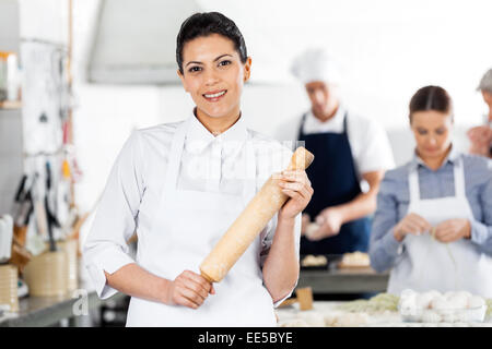 Smiling Chef Holding Rolling Pin While Colleagues Preparing Past Stock Photo