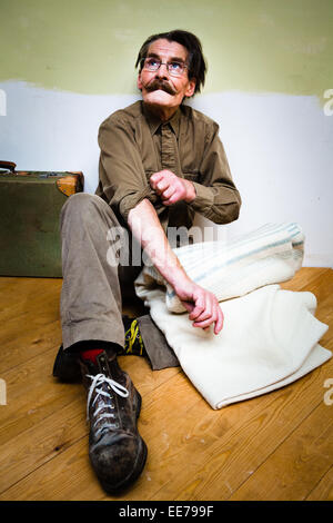 Man in his 60s with moustache wearing khaki shirt and trousers sitting on the floor. Stock Photo