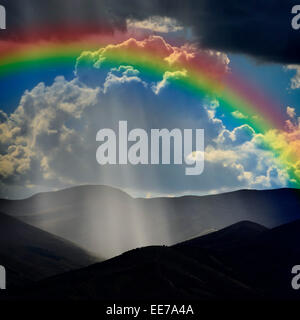 Sunlight rays from clouds falling on dark mountain range with Rainbow Stock Photo