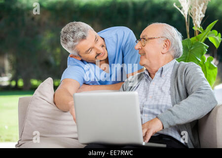 Smiling Nurse Assisting Senior Man In Using Laptop Stock Photo