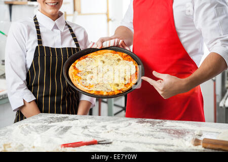 Chefs Presenting Delicious Pizza At Commercial Kitchen Stock Photo