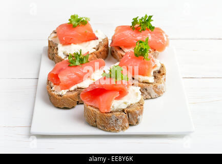 Sandwiches with salmon on white plate on wooden table Stock Photo