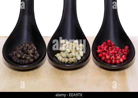 Three types of peppercorns on black spoons Stock Photo