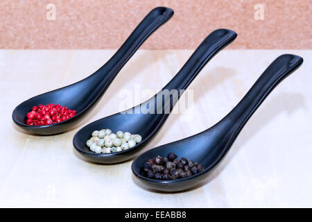 Three types of peppercorns on black spoons Stock Photo