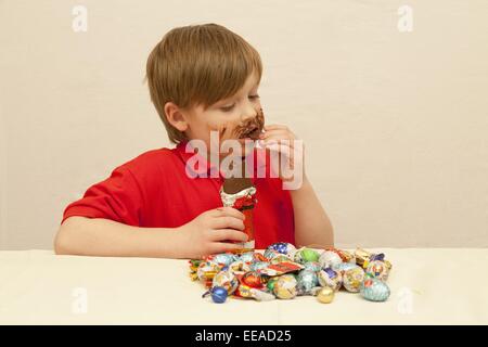 young boy with a pile of Christmas sweets in front of him eating chocolate Stock Photo