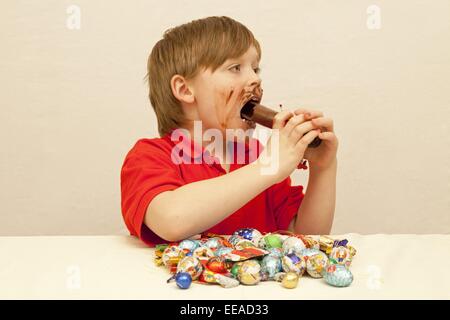 young boy with a pile of Christmas sweets in front of him eating a chocolate Santa Stock Photo