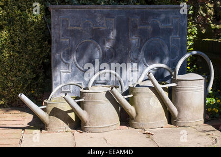 LEAD WATER TANK WITH FOUR METAL WATERING CANS IN GARDEN Stock Photo