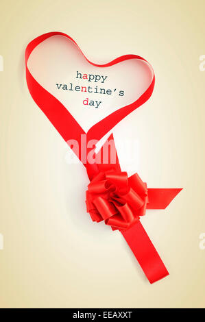 a red ribbon forming a heart and the text happy valentines day written on a beige background Stock Photo