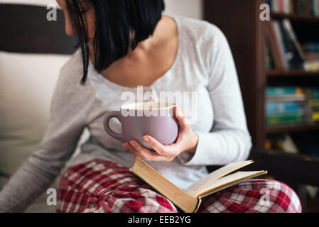 Women in her living room reading book and drinking tea Stock Photo