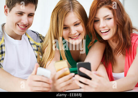 three smiling students with smartphone at school Stock Photo