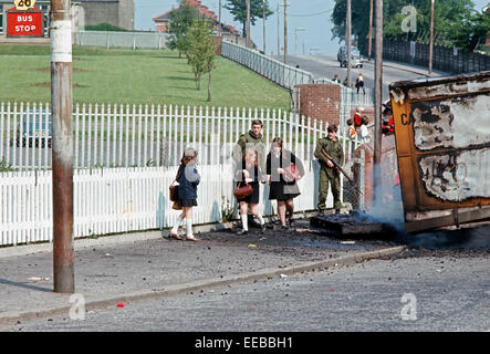 BELFAST, NORTHERN IRELAND - JUNE 1972. School Children passing in front of British Army Soldiers and Burning Hijacked vehicle, West Belfast during The Troubles, Northern Ireland, Stock Photo