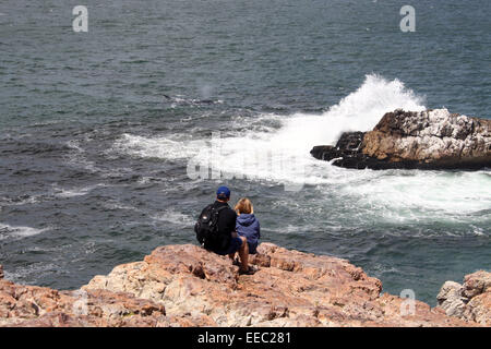 Tourists sitting on the cliffs at Hermanus watching a Southern Right Whale Stock Photo