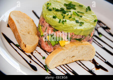 Raw salmon chopped and mixed with pepper and onion sour cream, Avocado cream and chives as garnish and toasted bread Stock Photo