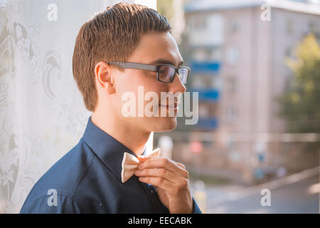 Portrait of young groom tying bow tie while getting ready for wedding Stock Photo