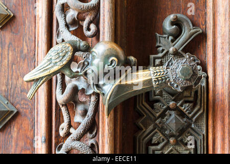 An ornate doorhandle of a castle where an asian man's head is pecked by a bird Stock Photo