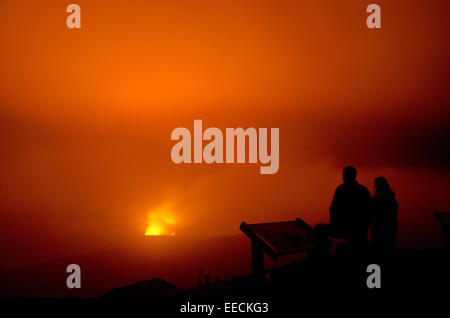 Tourists view smoke and fire from the Halemaumau crater within the much larger summit caldera of Kīlauea volcano from Jaggar Museum Overlook on a foggy evening in Hawaii Volcanoes National Park in Hilo, Hawaii. Stock Photo