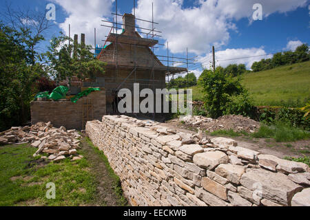 Renovation and new built dry stone wall constructed of new Cotswolds stone using traditional method at period property, UK Stock Photo