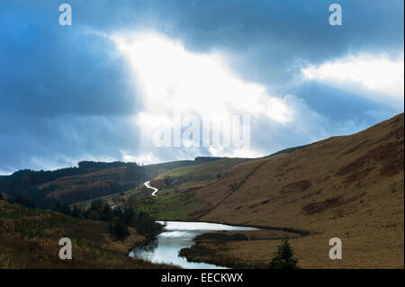 Sunlight through cloud shining on river and empty road along a valley in the Brecon Beacons mountain range in Wales, UK Stock Photo