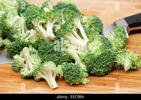 Chopped up broccoli with chef knife laying on a wood cutting board. Stock Photo