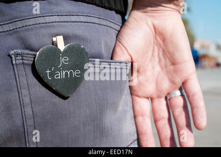 a heart-shaped chalkboard with the text je t aime, I love you written in french, in the back pocket of the trousers of a young m Stock Photo