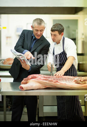 A manager teaching a trainee butcher how to cut meat Stock Photo