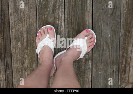 Feet on unfinished wood surface in pair of sandals Stock Photo