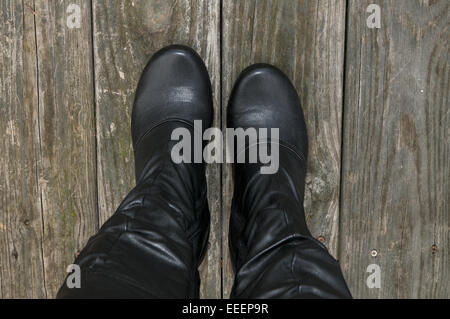 Woman's feet wearing high black boots on an unfinished wood.