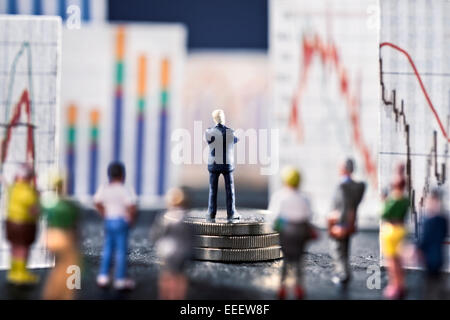 Banker looks on boards with various charts, symbolizing the ups and downs in the markets. He stands on a base of coins. Stock Photo