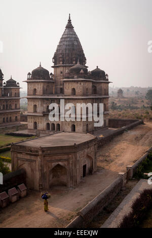 Woman carrying hay bale on head in front of cenotaph, Orchha, Madhya Pradesh state, India Stock Photo