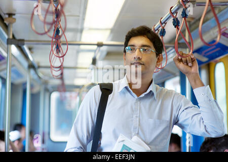 Asian Indian businessman taking ride to work, standing inside train. Stock Photo