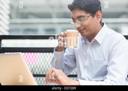 Asian Indian businessman using laptop computer while drinking a cup hot milk tea. Stock Photo