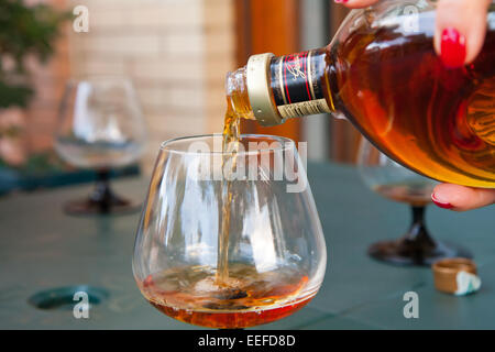 A women holding a glass of brandy standing on a patio on a sunny day Stock Photo