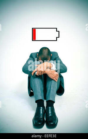 a young businessman curled up in the floor with his head between his knees and an illustration of a low battery Stock Photo